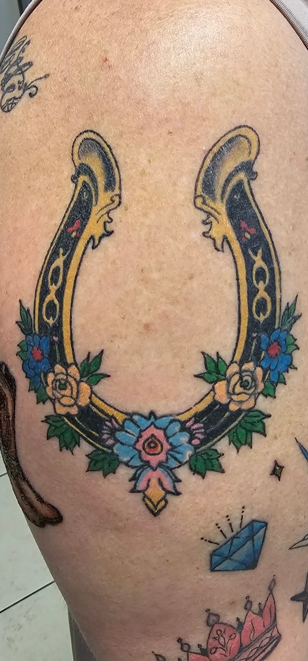 A colorful horseshoe tattoo on skin, decorated with flowers, stars, and decorative patterns.