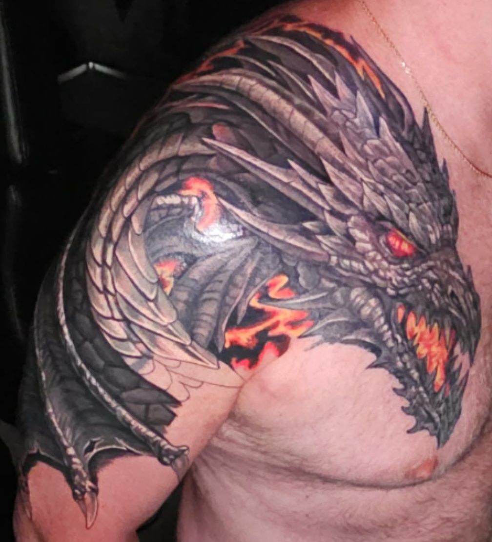 Large black dragon tattoo with red eyes and orange accents on a person’s upper arm and shoulder