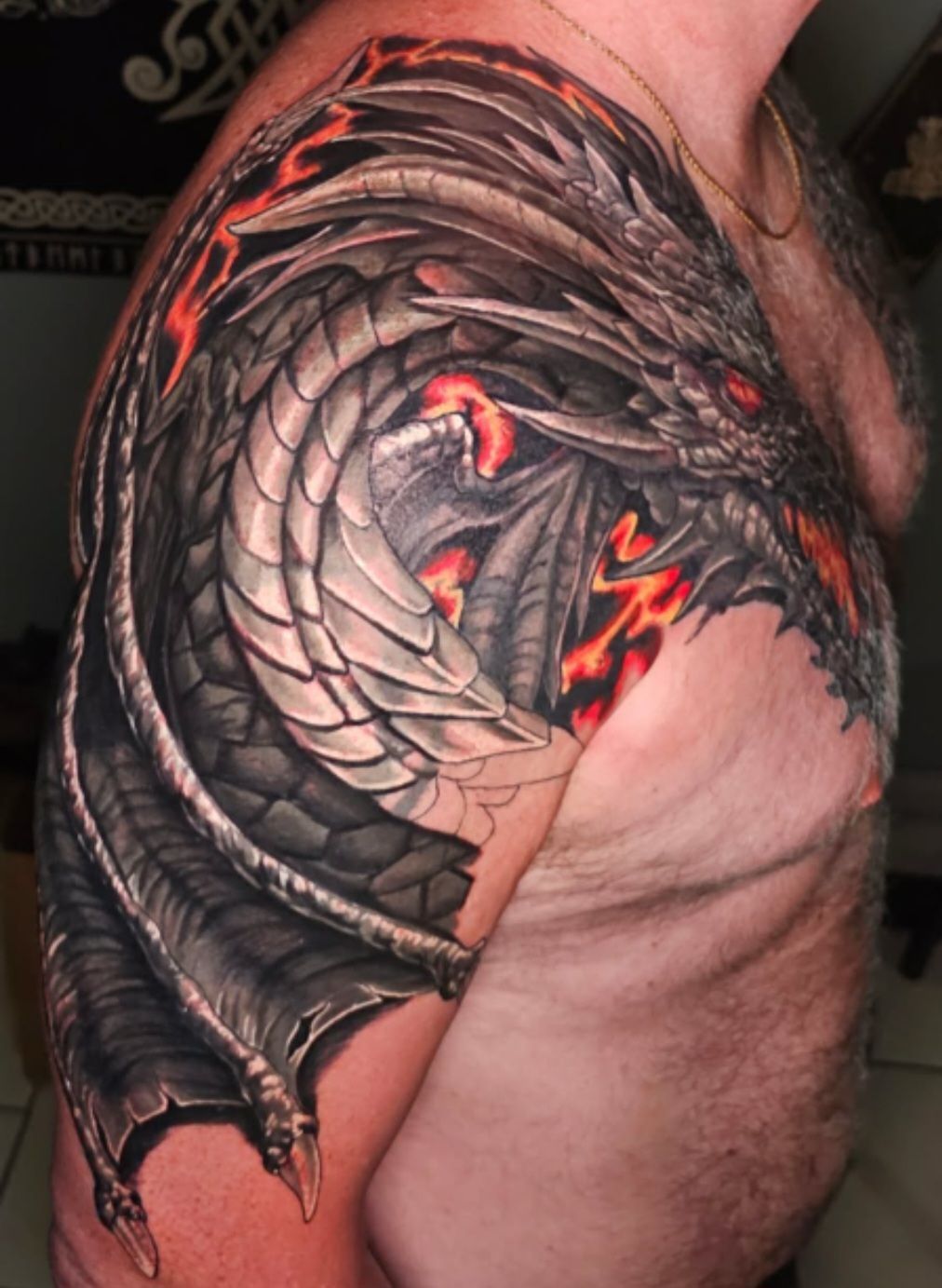 Detailed dragon tattoo on a person’s shoulder and upper arm, black and gray with red accents