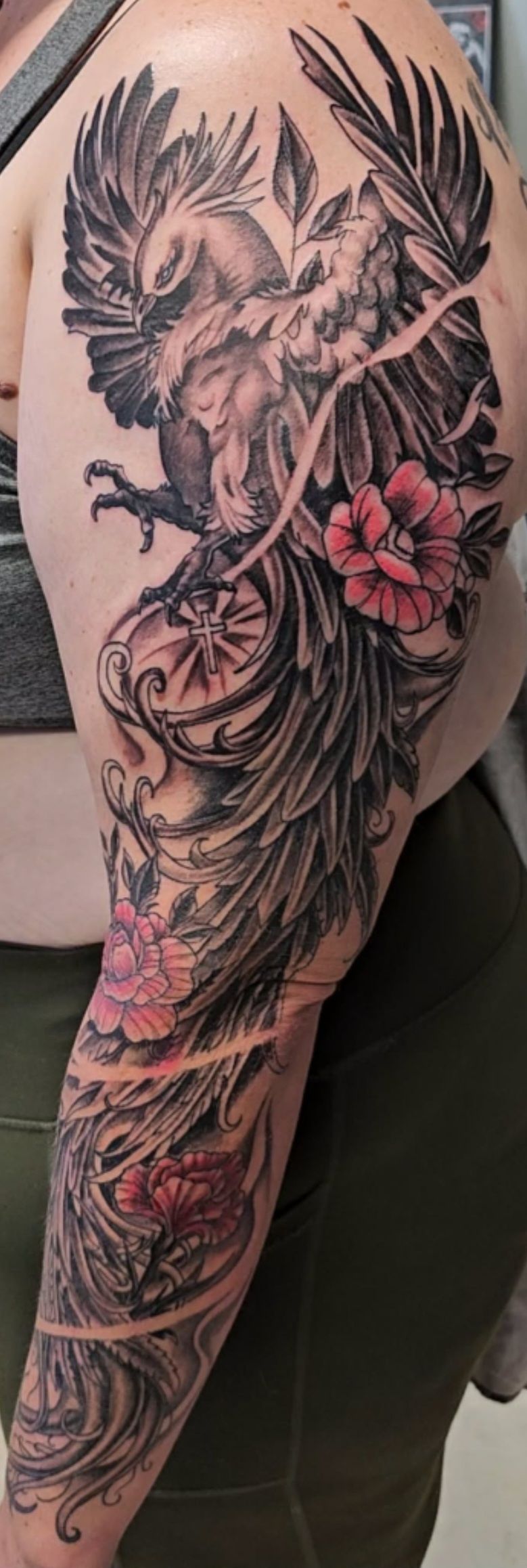 Arm tattoo with a black-and-gray dragon and pink flowers on a person’s upper arm and forearm