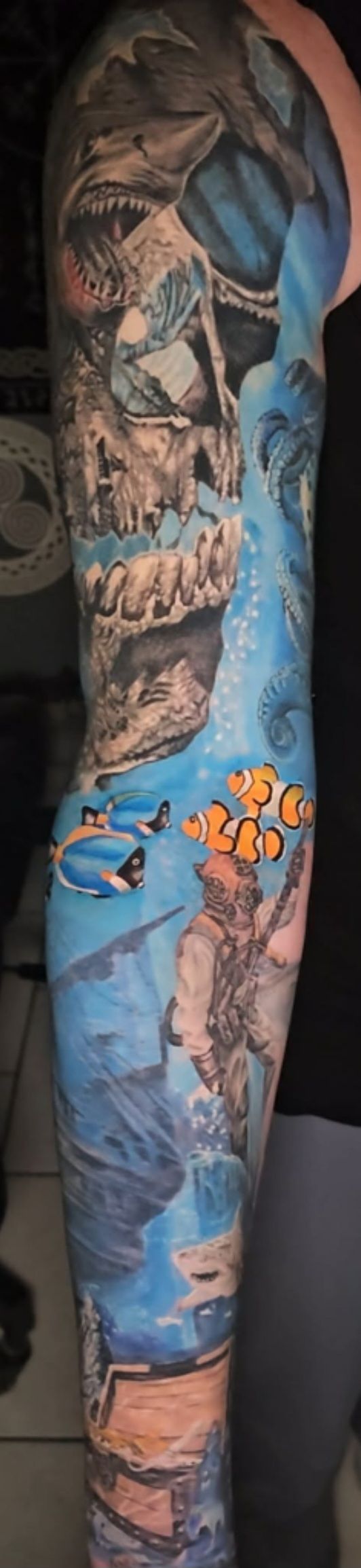 Tattooed arm with colorful dragon and fantasy scene sleeve tattoo against a dark background