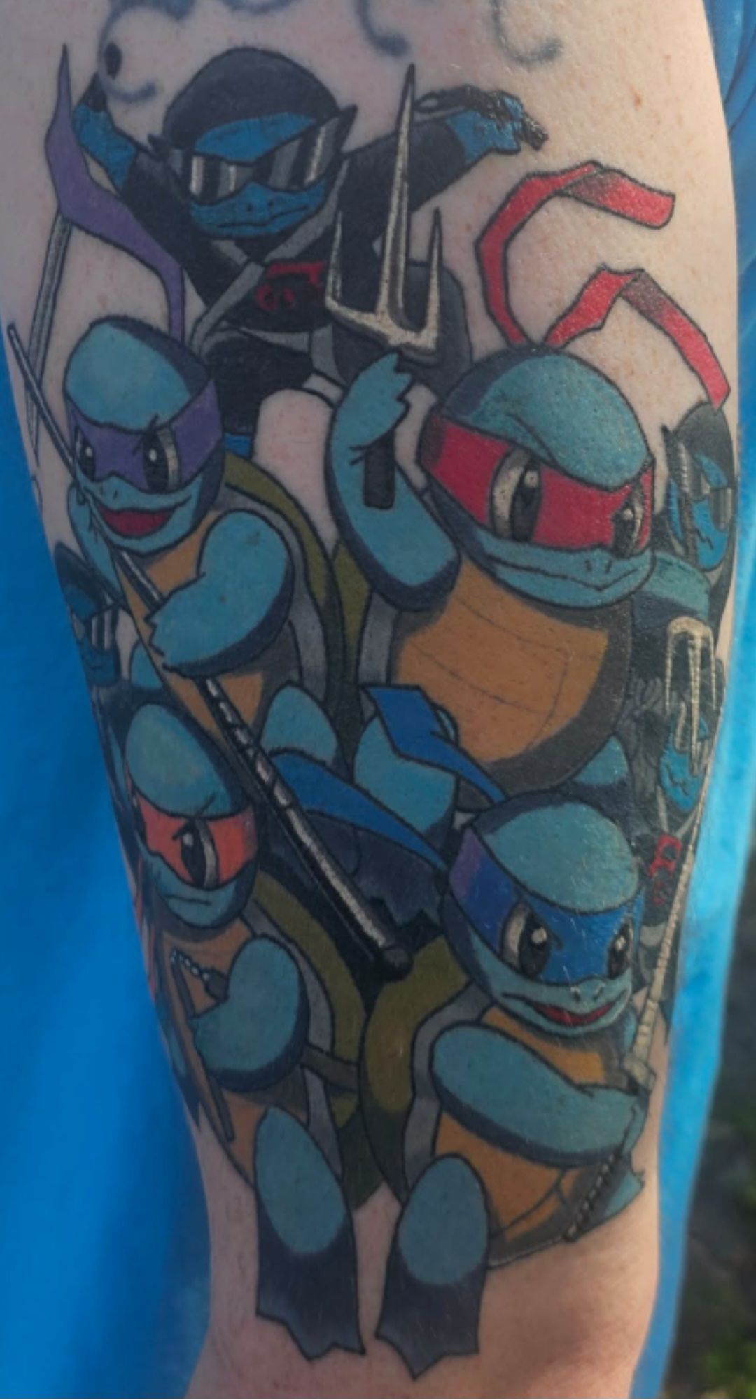 Colorful tattoo of Teenage Mutant Ninja Turtles on an arm, showing several blue-masked characters in action.