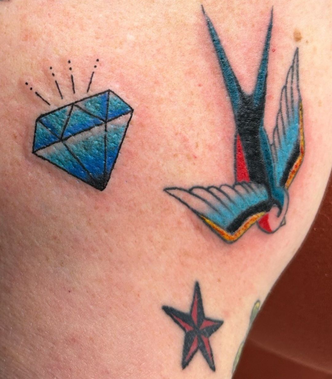 Blue diamond, colorful swallow, and star tattoos on skin