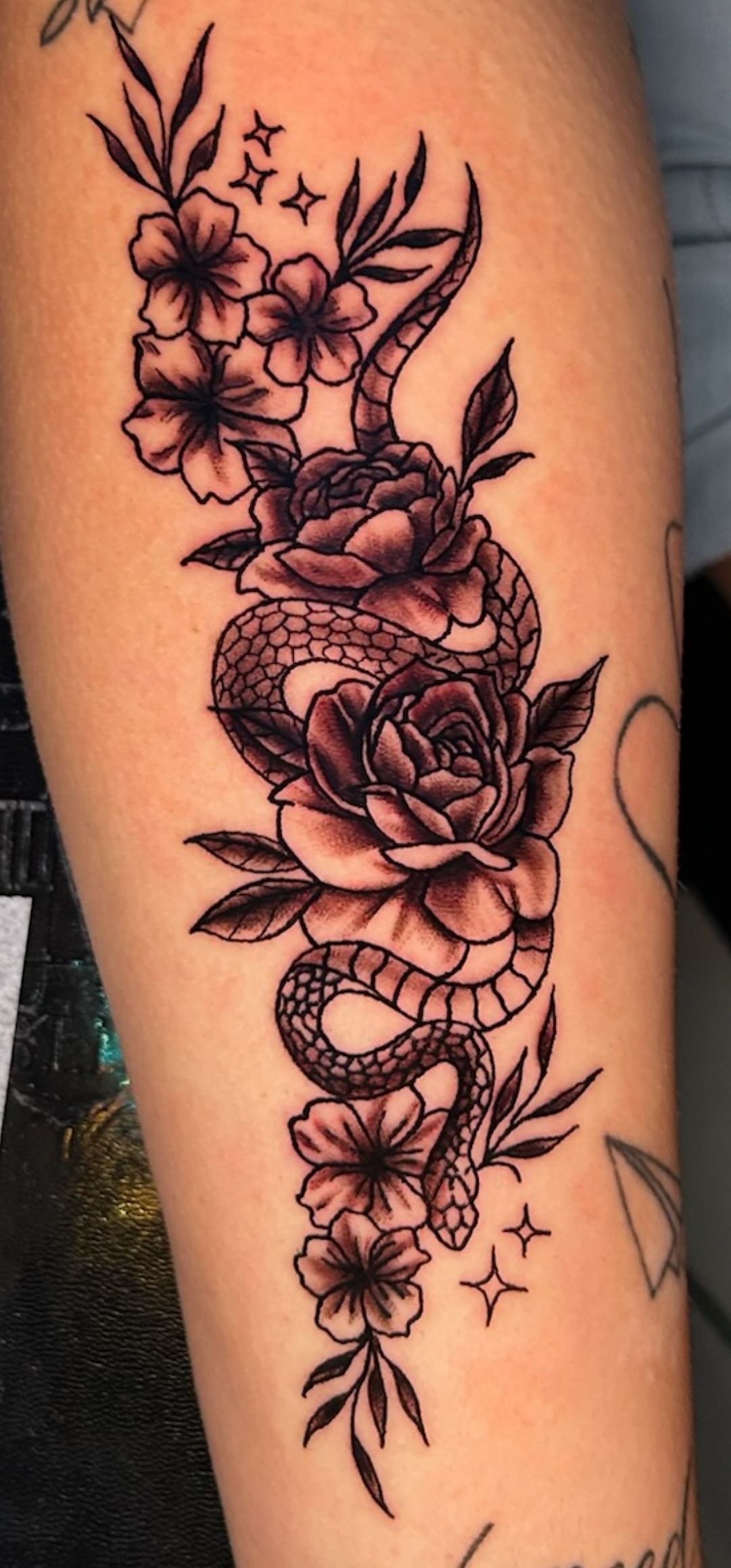 Black floral and snake tattoo with roses and stars on an arm.