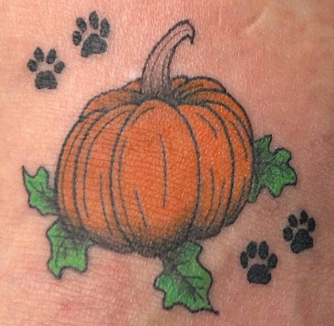 Orange pumpkin tattoo with green leaves and black paw prints around it