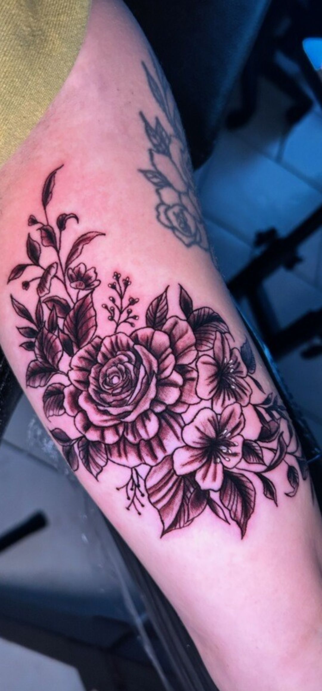 Close-up of a forearm with a black floral tattoo of roses and leaves