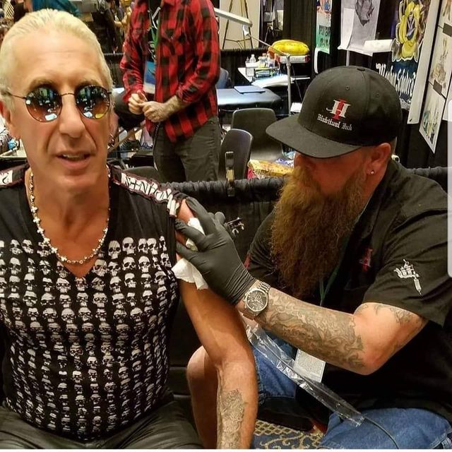 A man with a beard is getting a tattoo on his arm