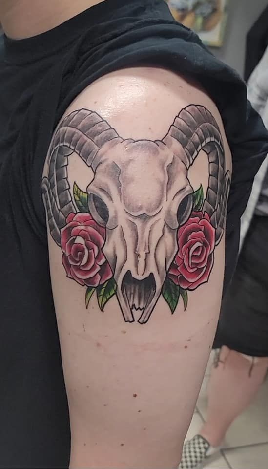 A person has a tattoo of a ram skull with horns and roses on their arm.