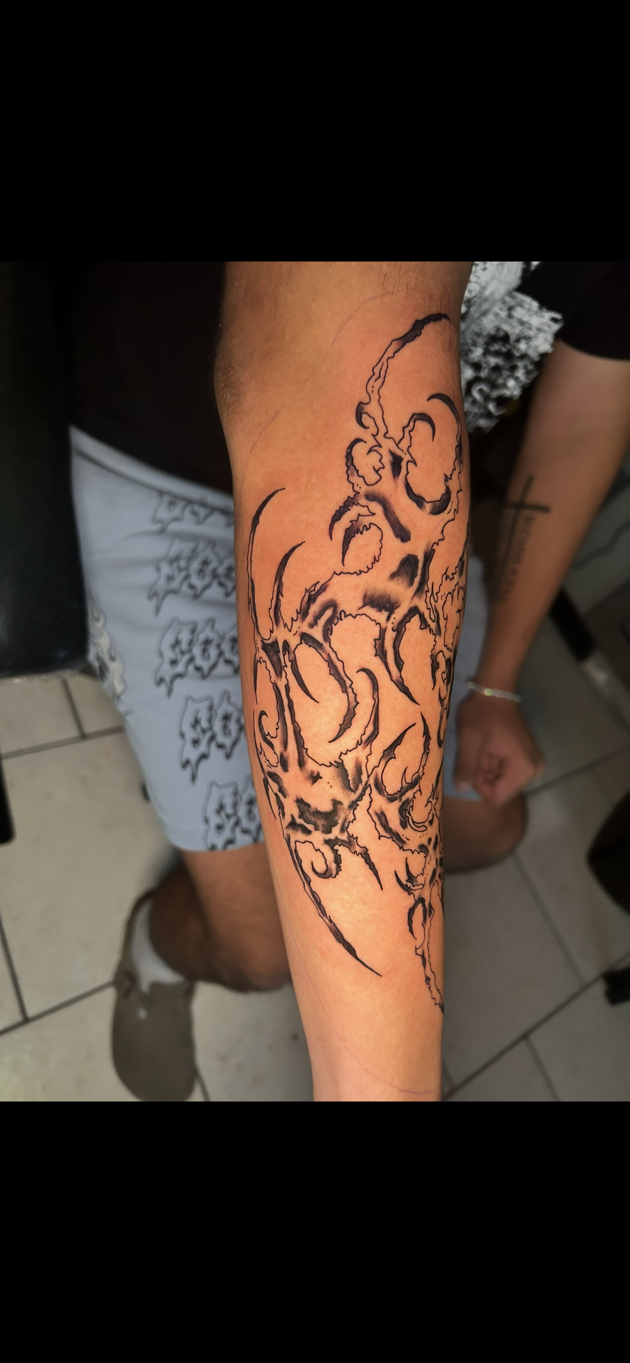 Arm with a large, black tribal tattoo. Person in shorts and shirt, indoors.