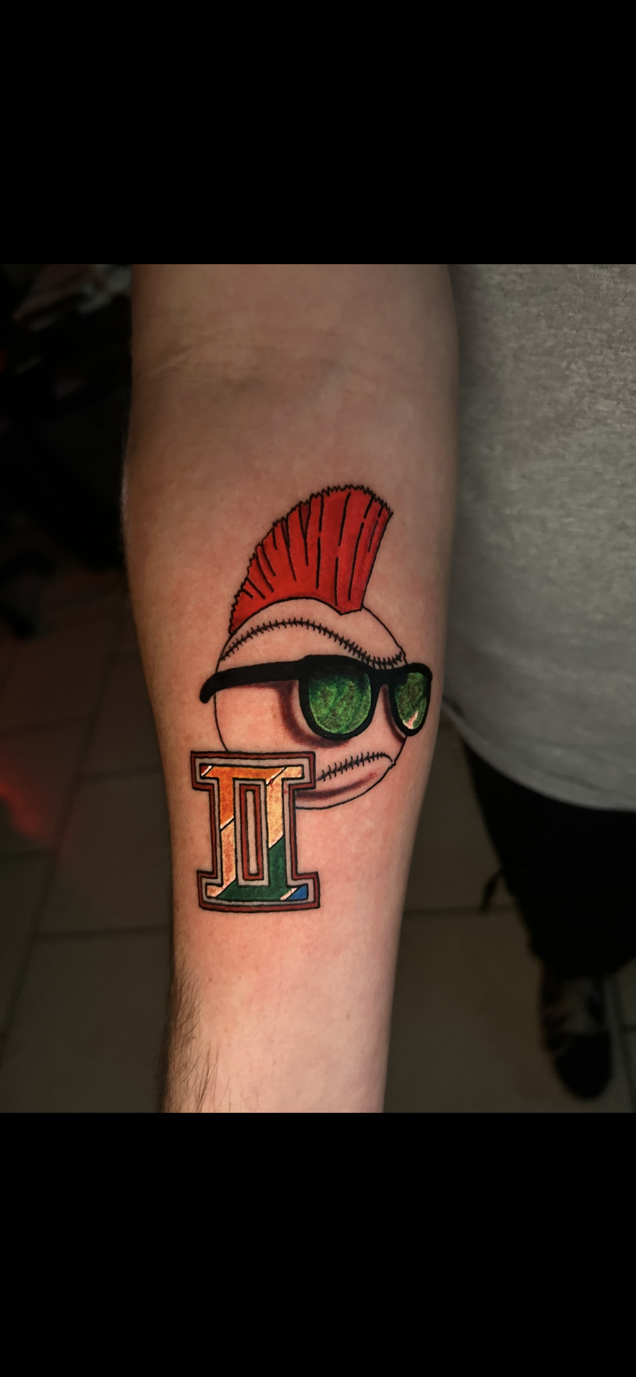 Tattoo of a baseball with a mohawk and sunglasses, with a 