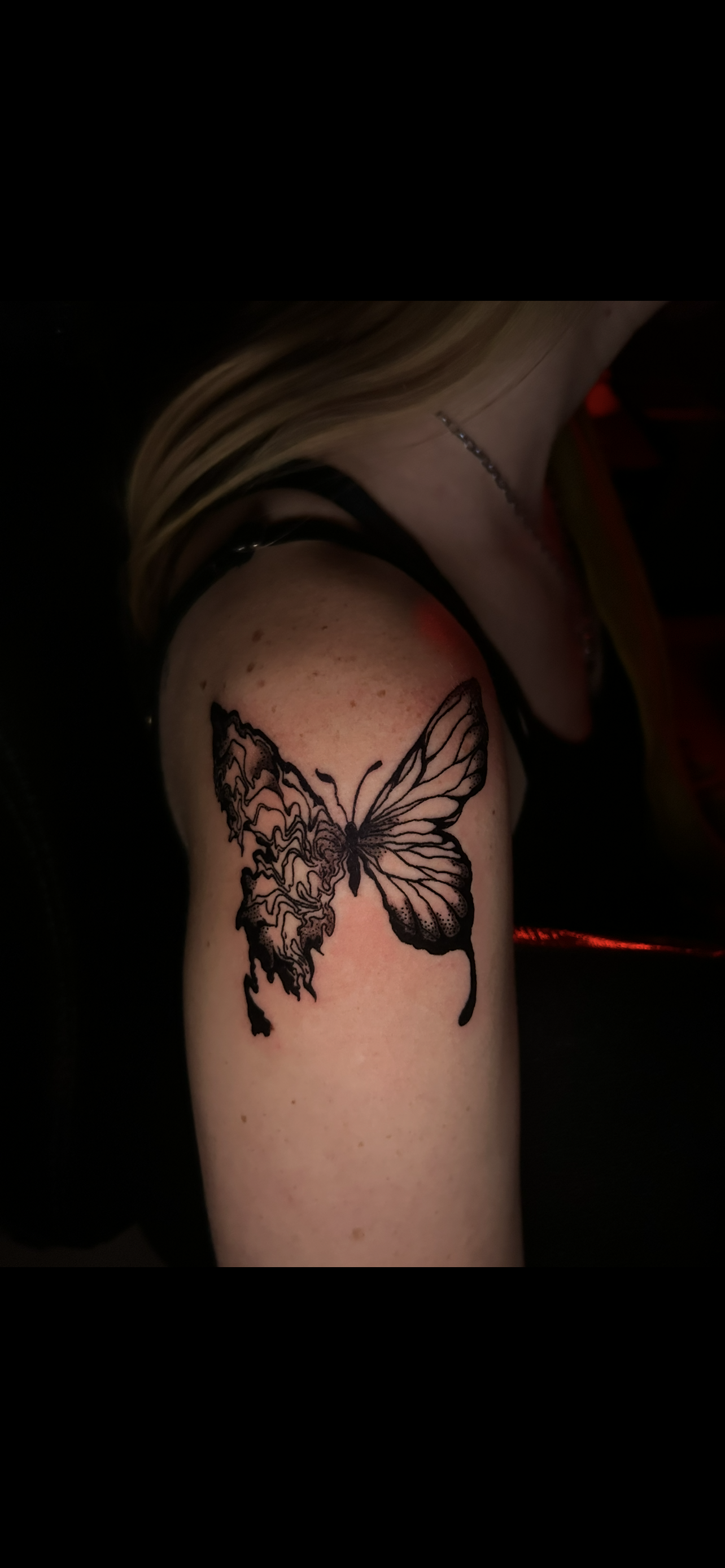 A butterfly tattoo on a person's upper arm. One side of the butterfly is detailed while the other is more abstract.