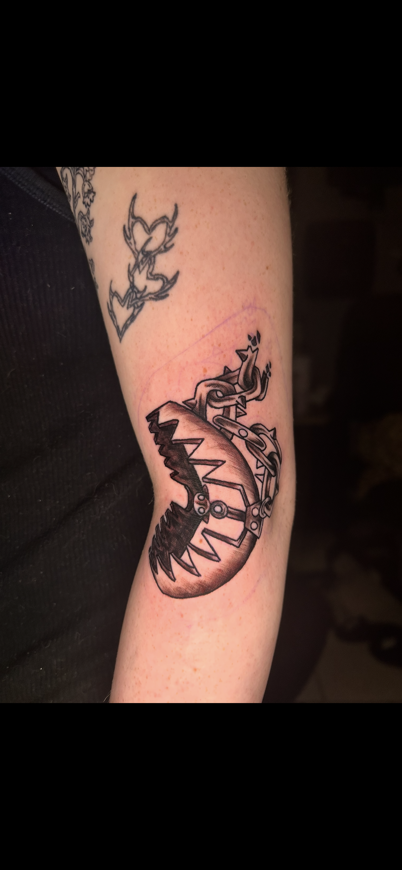 Tattoo of a stylized insect or mechanical object on a person's forearm, with a smaller tattoo nearby.