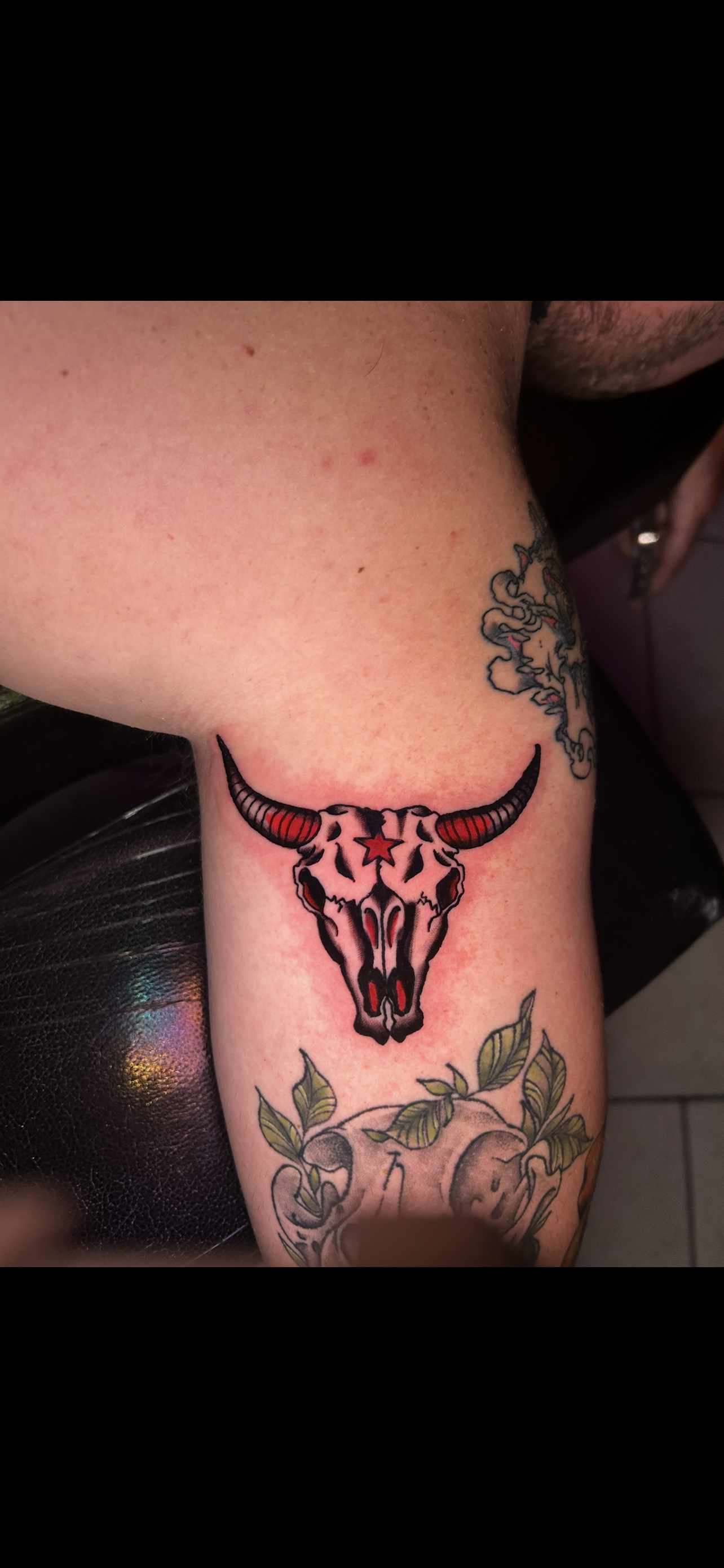 Tattoo of a pixelated bull skull with red accents on a person's arm, also other flower tattoos.