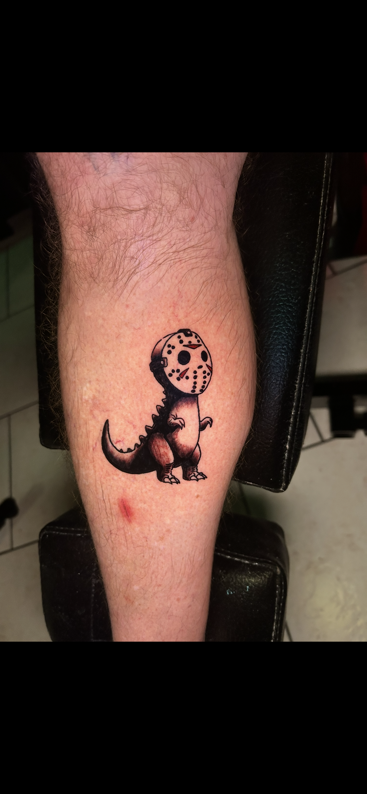 Tattoo of a pixelated dinosaur wearing a hockey mask on a leg.
