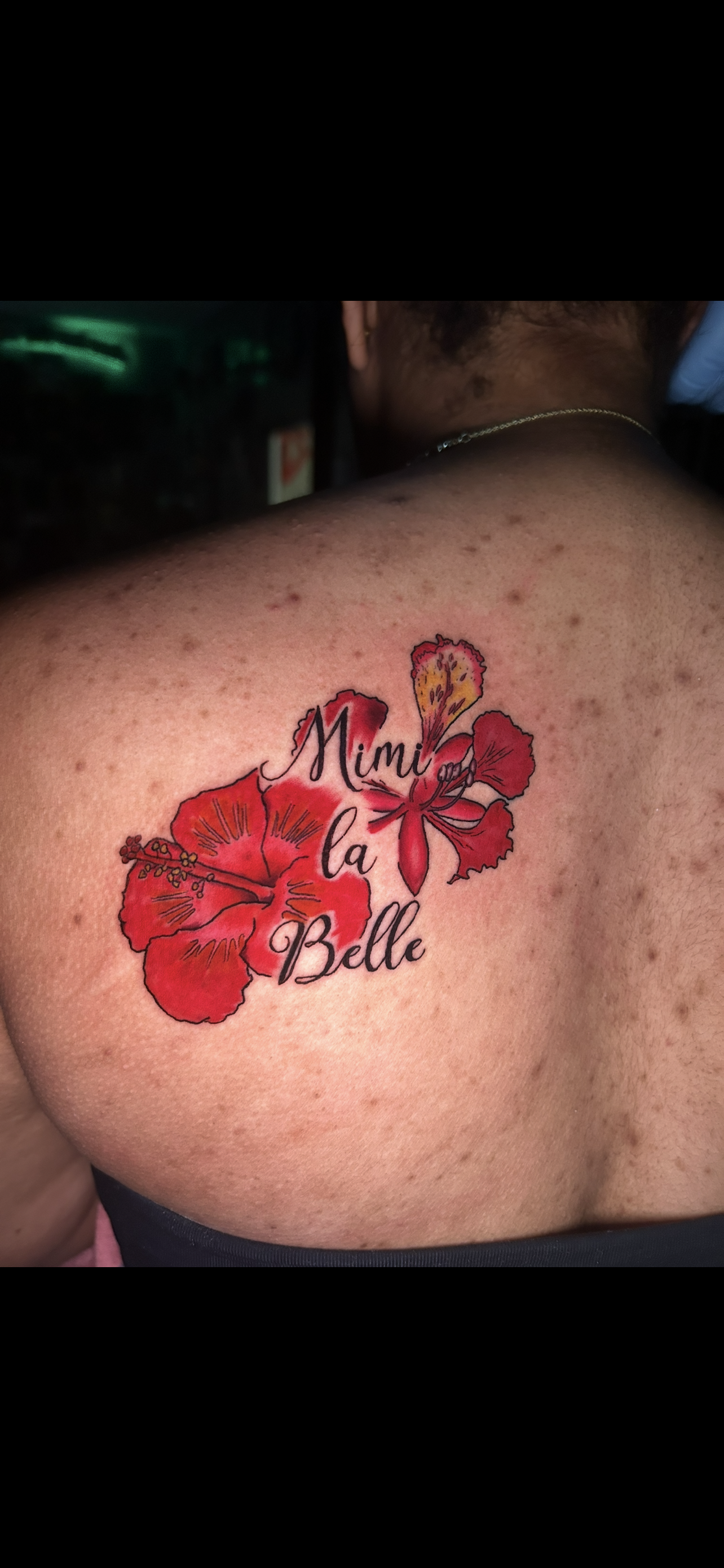 Tattoo on a person's shoulder with red flowers and script that says 