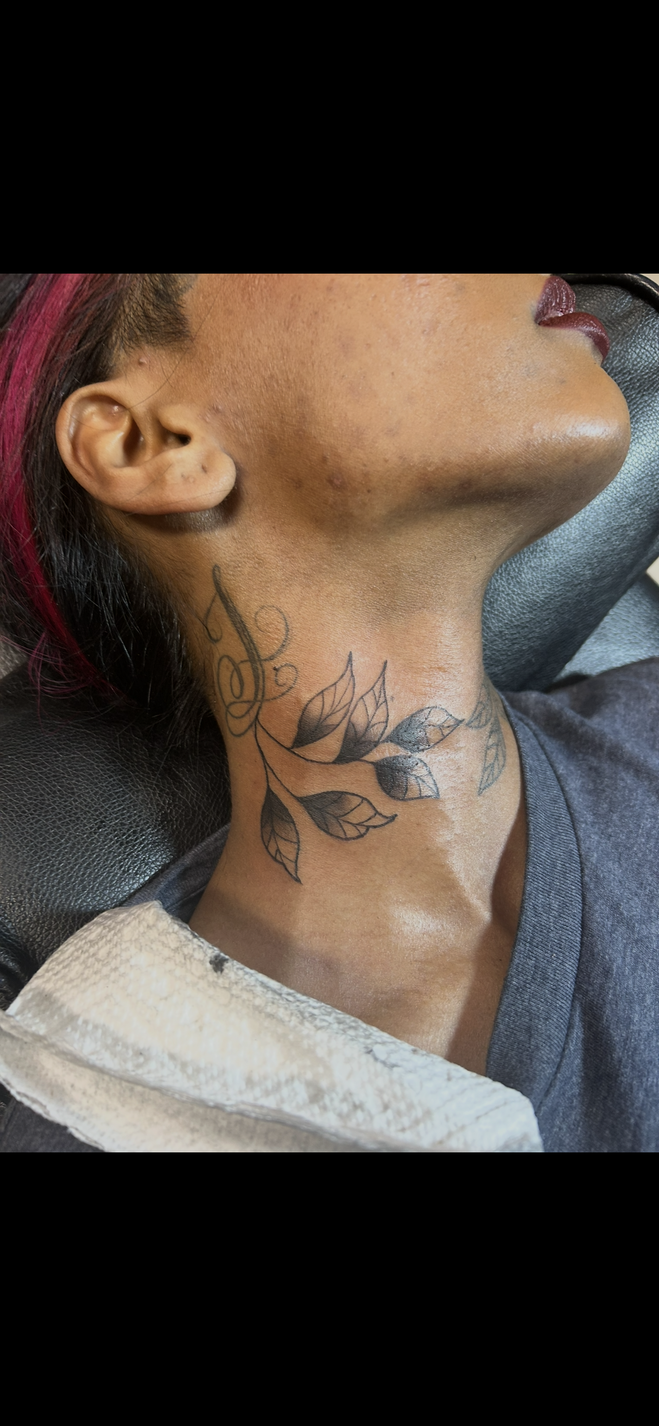 Person with a neck tattoo of leaves and flowers. They are wearing a gray shirt.