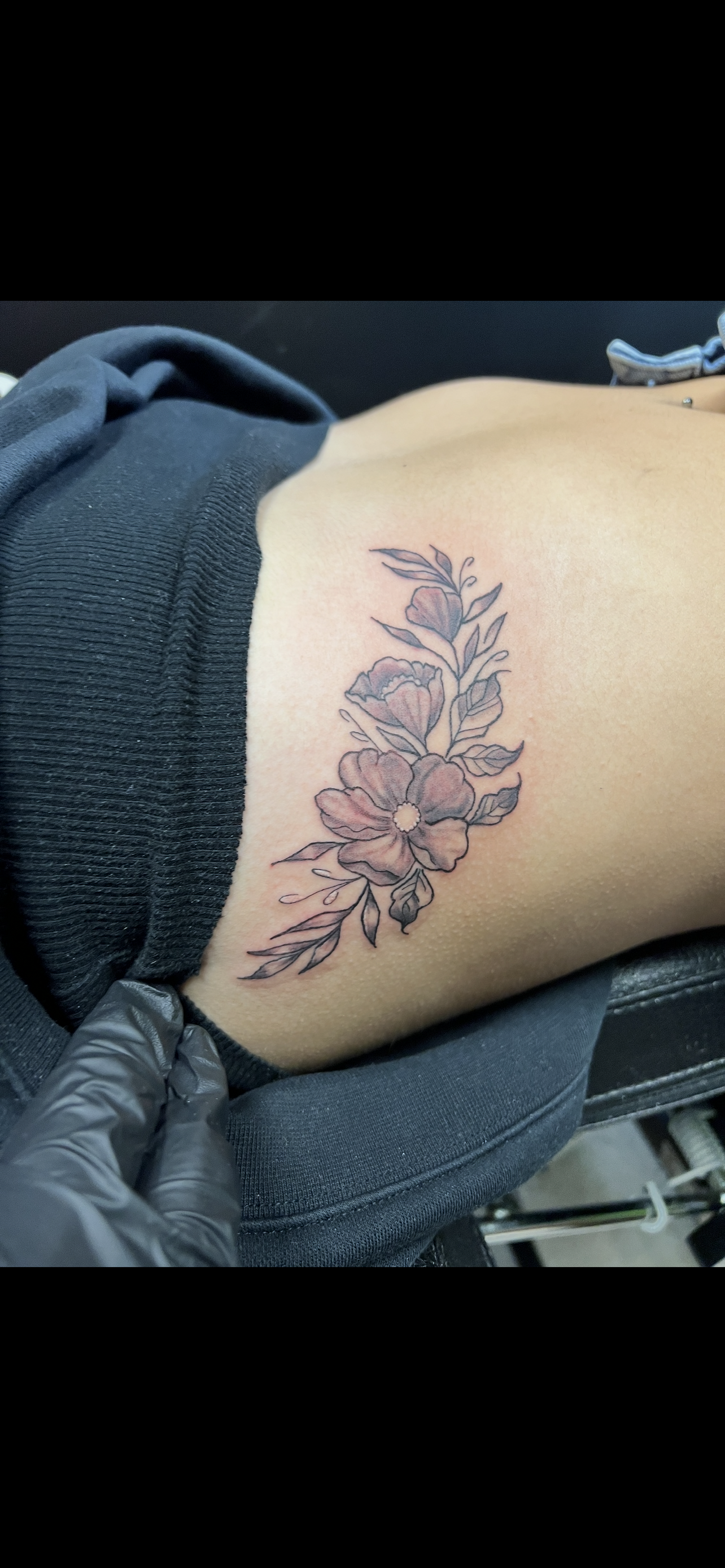 Floral tattoo on arm. A gloved hand is visible, possibly tattooing.