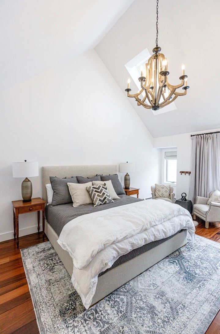 Bright bedroom with a gray bed, gold chandelier, and white vaulted ceiling.