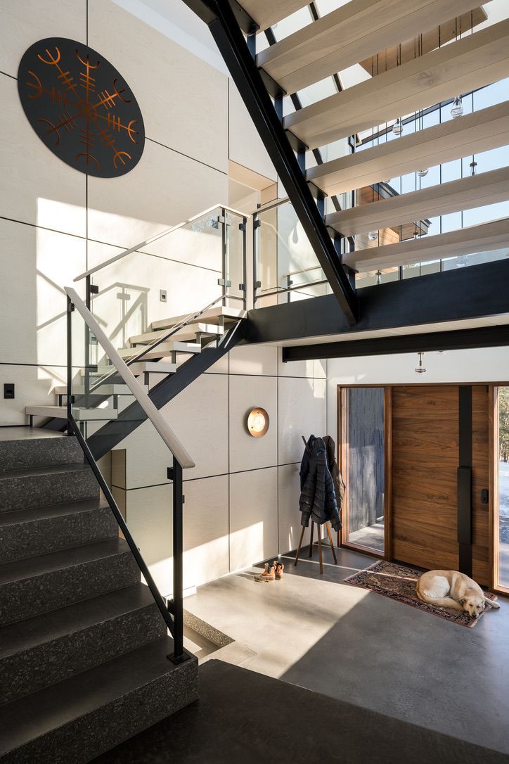 Modern indoor staircase with black railings, white walls, and a wooden front door in a bright entryway