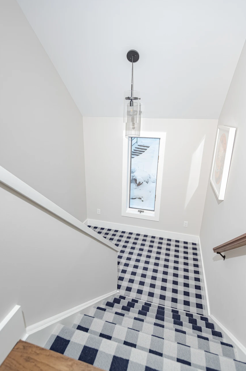 Stairwell with blue-and-white checkered carpet leading to a bright window and hanging pendant light