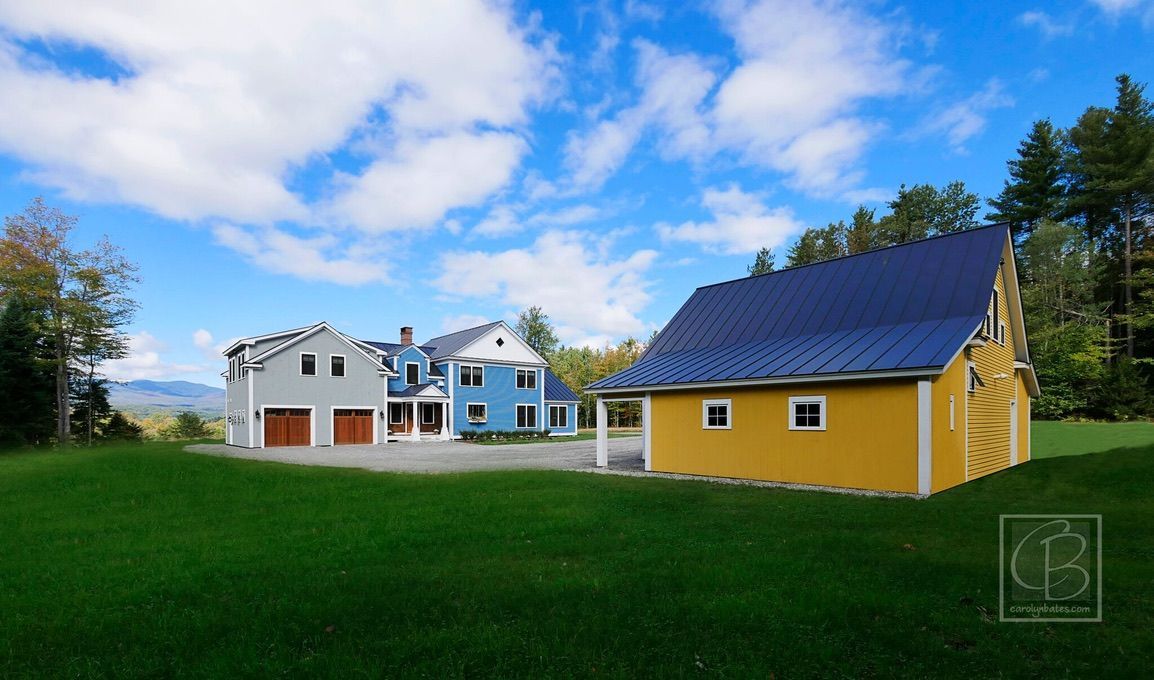 Colorful houses and garage beside a grassy field under a blue sky with clouds