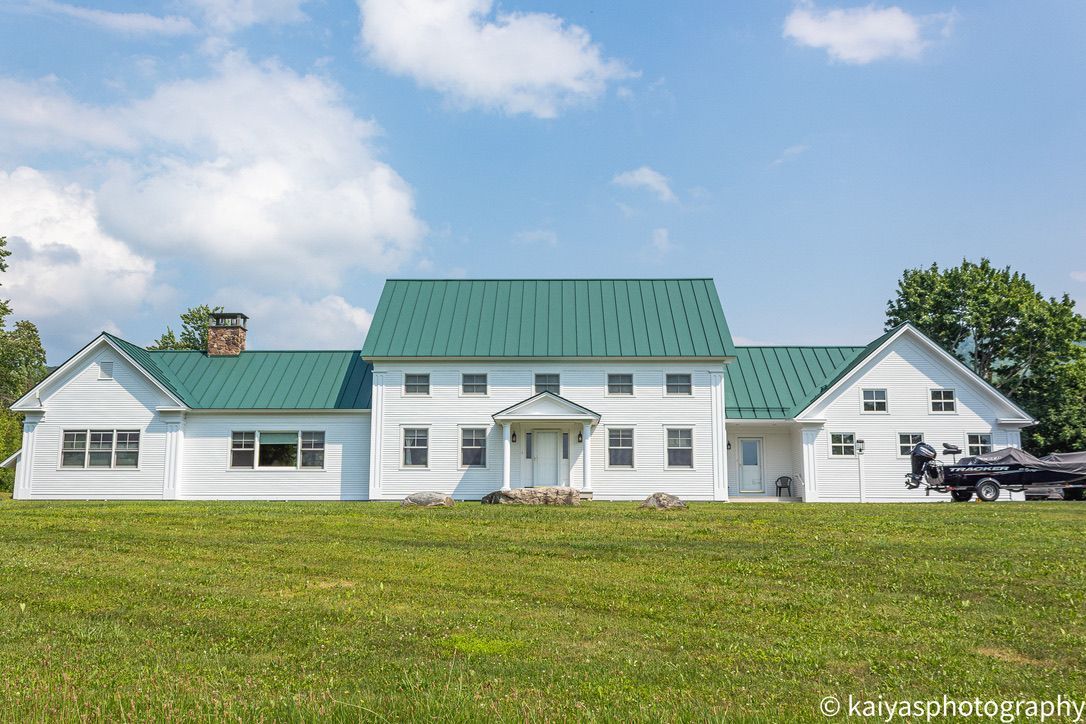 White house with green roof and lawn under a blue sky with clouds