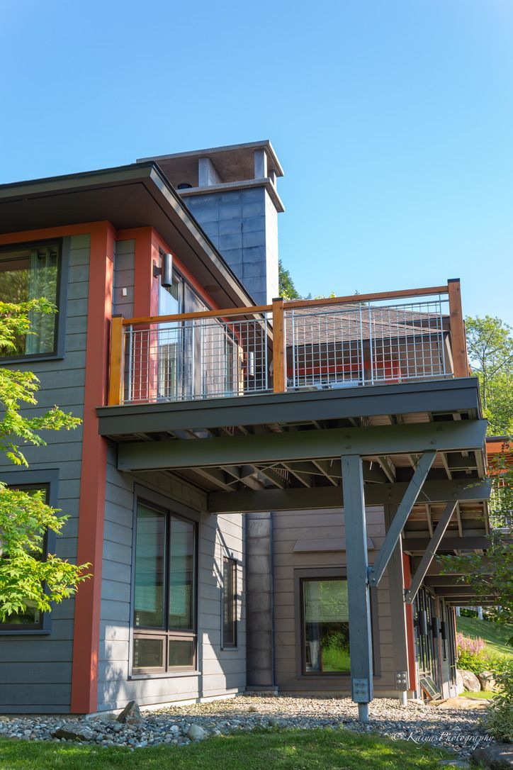 Modern house exterior with raised wooden deck, metal railing, and support beams