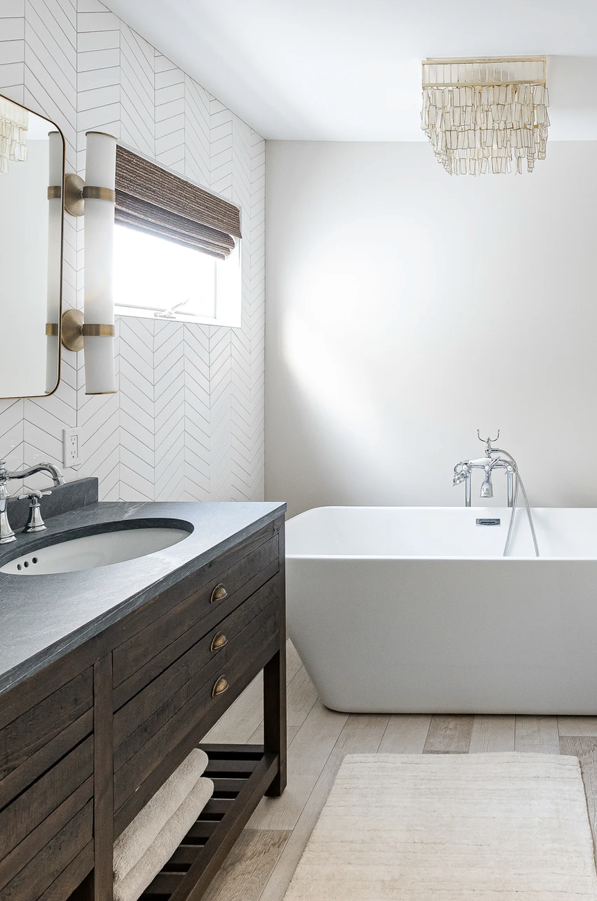 Bright modern bathroom with a dark vanity, white tub, and window blinds.