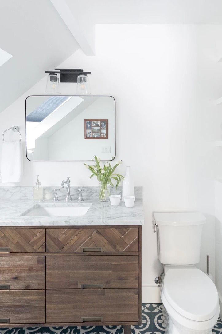 Bright white bathroom with wood vanity, sink, mirror, and toilet under a skylight.