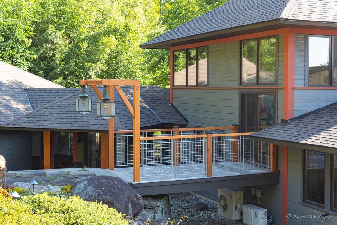 Modern house with deck, orange trim, and large windows surrounded by trees and rocks