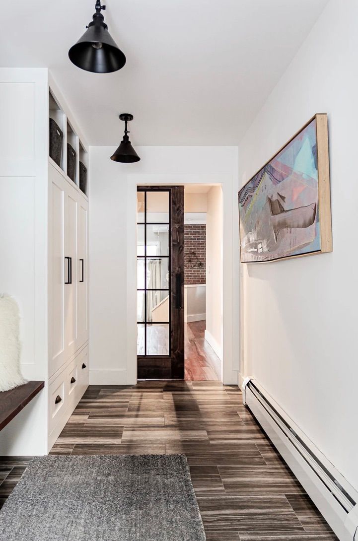 Bright narrow hallway with white walls, black pendant lights, wood floors, and a framed painting.