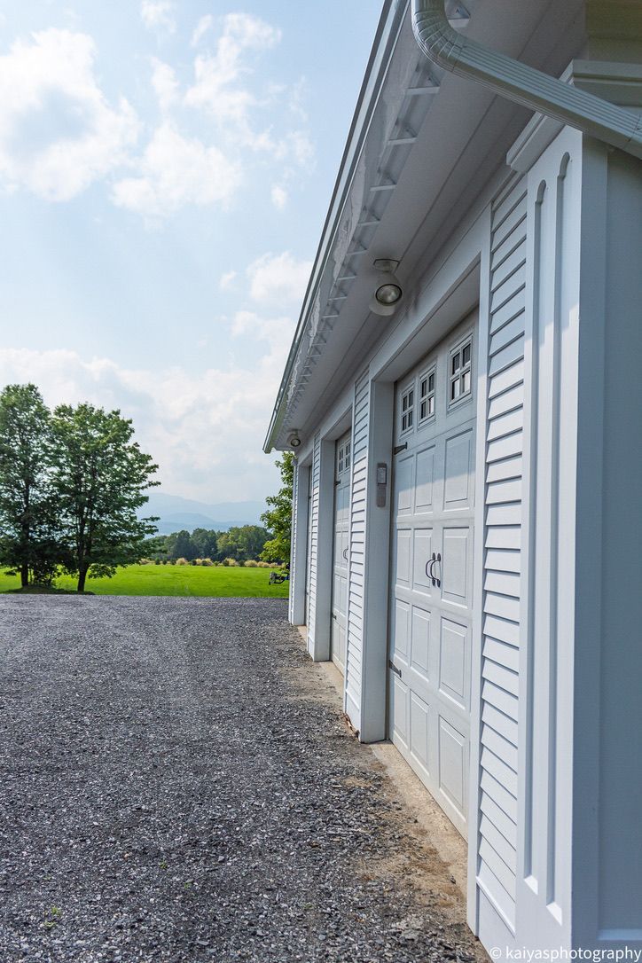 Dark blue house with black garage doors and dormer windows, seen from a driveway under a clear sky
