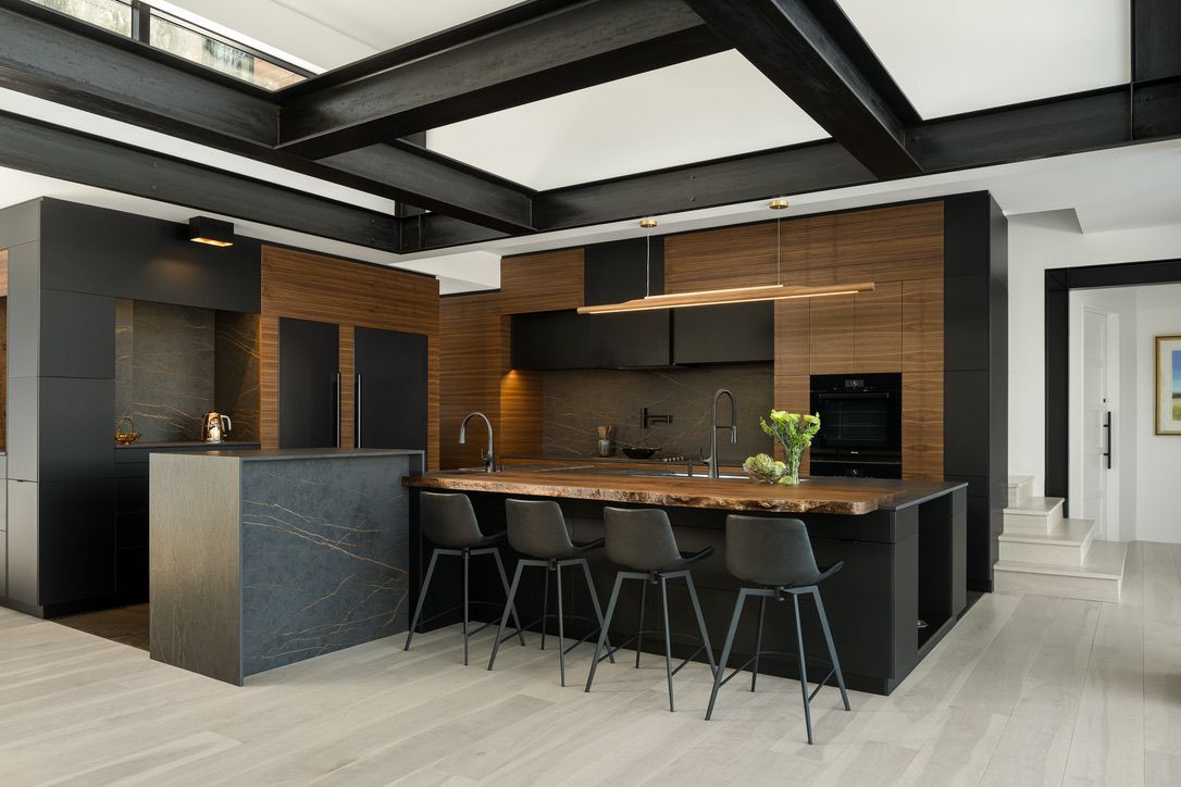Modern kitchen with dark cabinets, wood accents, island seating, and exposed black ceiling beams