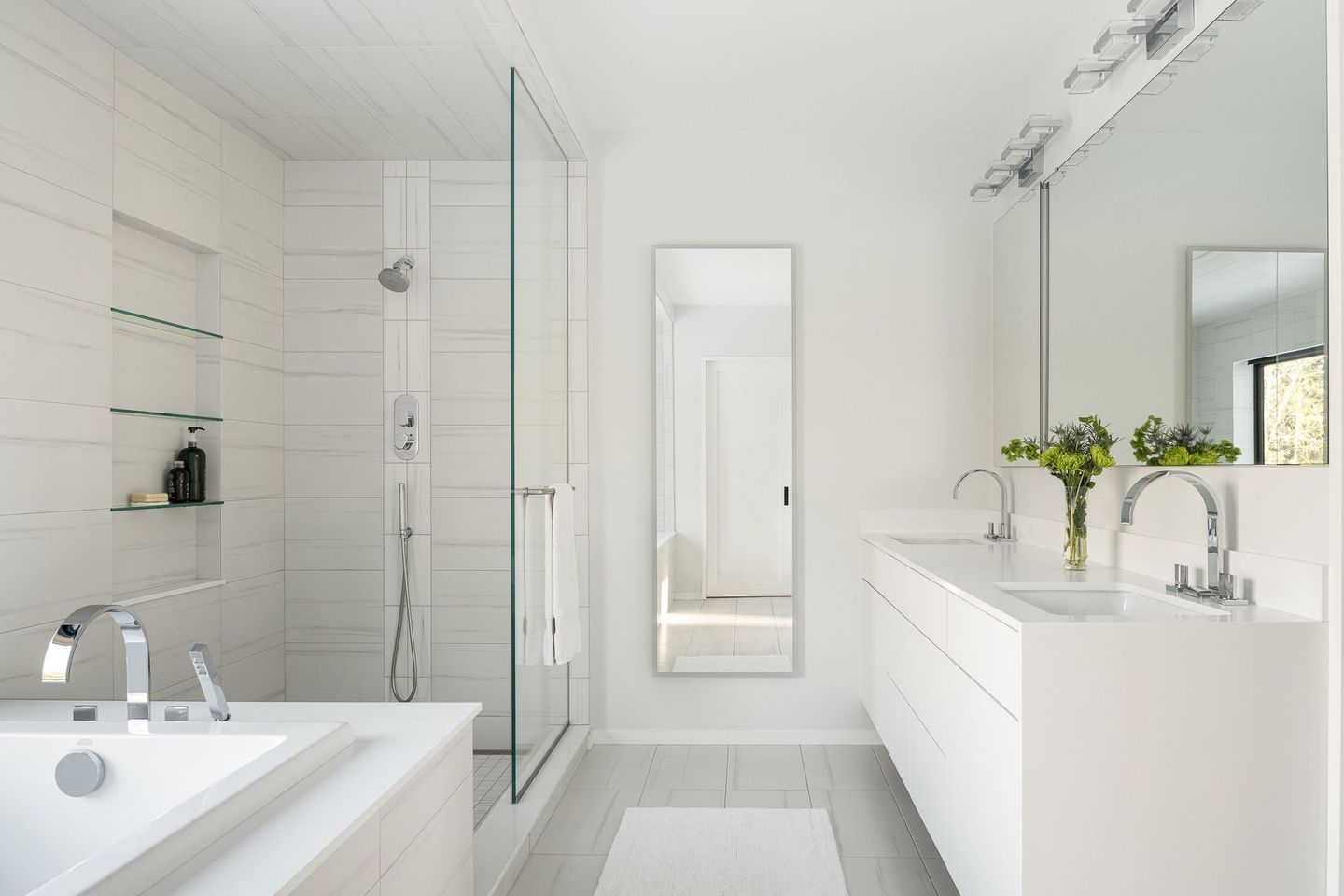Bright white modern bathroom with a tub, glass shower, large mirror, and vase of flowers on the vanity