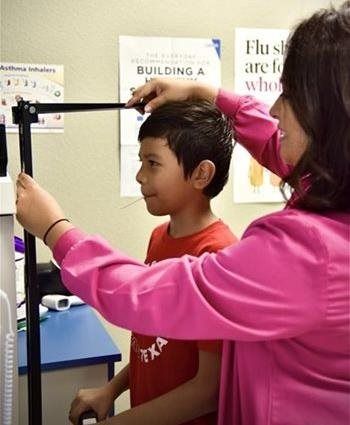 A person in pink measuring a child's height with a stadiometer in a medical setting.