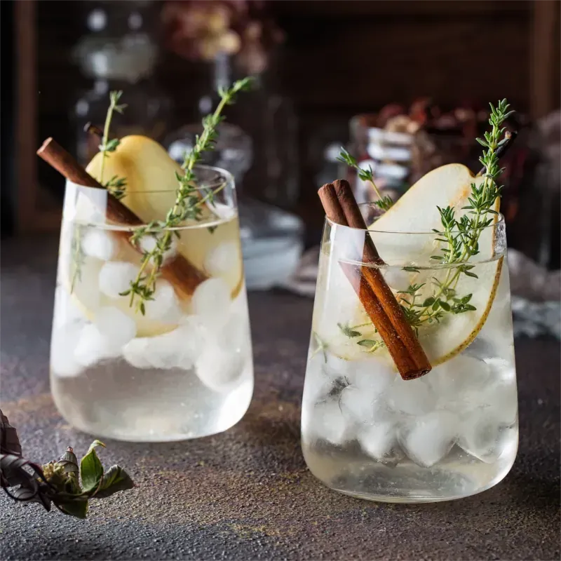 Zwei Cocktails mit Eis, Birnenscheiben, Zimtstangen und Thymian.