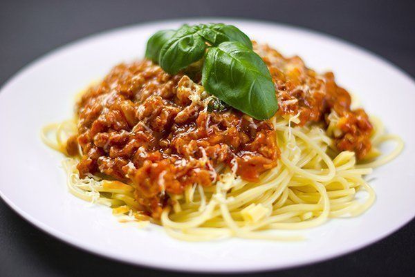 Spaghetti mit Fleischsoße, überbacken mit geriebenem Käse und Basilikum, auf einem weißen Teller.