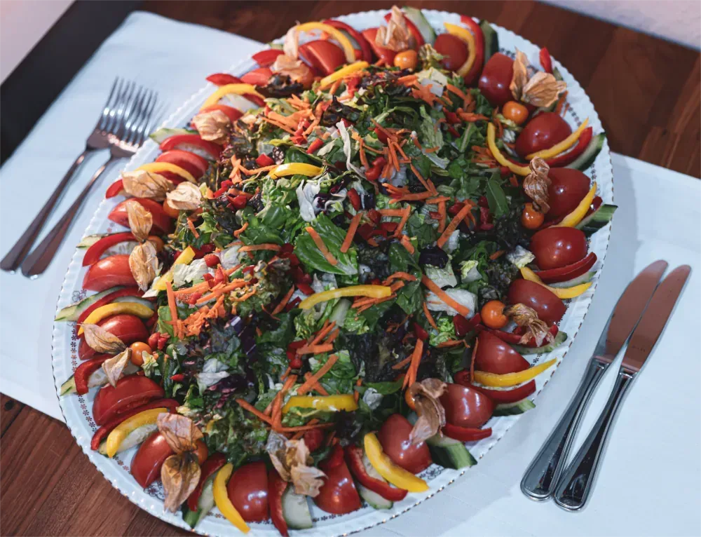 Ovale Platte mit buntem Salat: Tomaten, Paprika, Gurken und Blattgemüse.