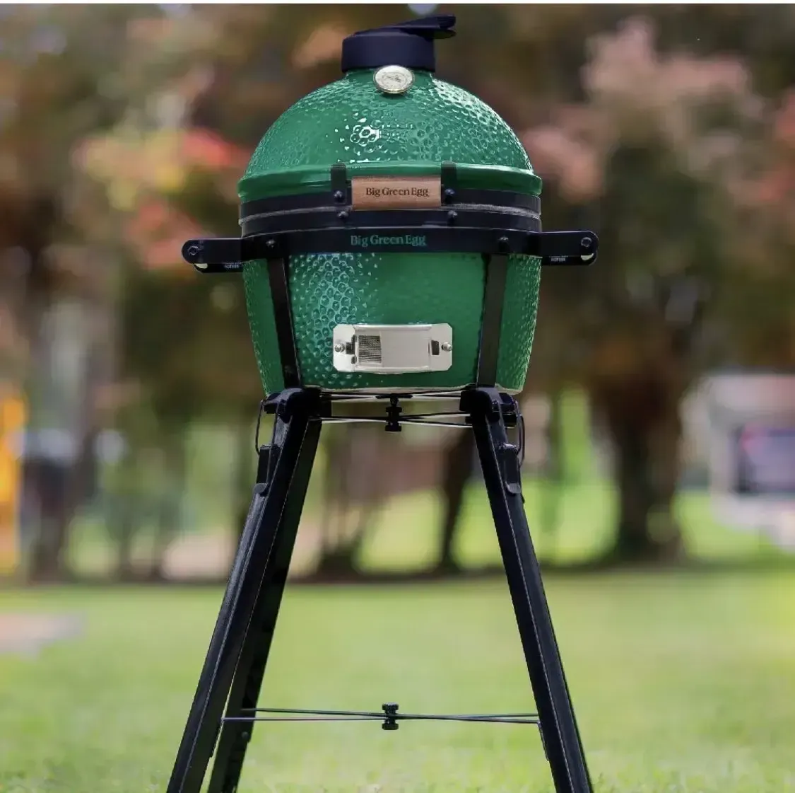 A green grill is sitting on a tripod in the grass.