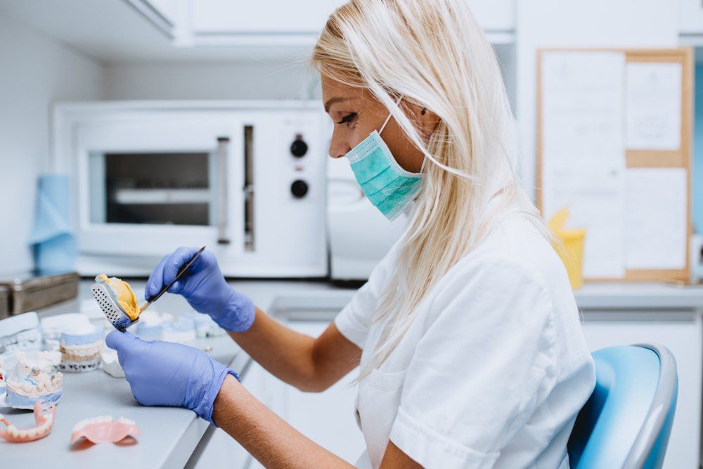 A Female Dentist is Working on a Denture in a Dental Office — Complete Denture Clinic in Kanwal, NSW