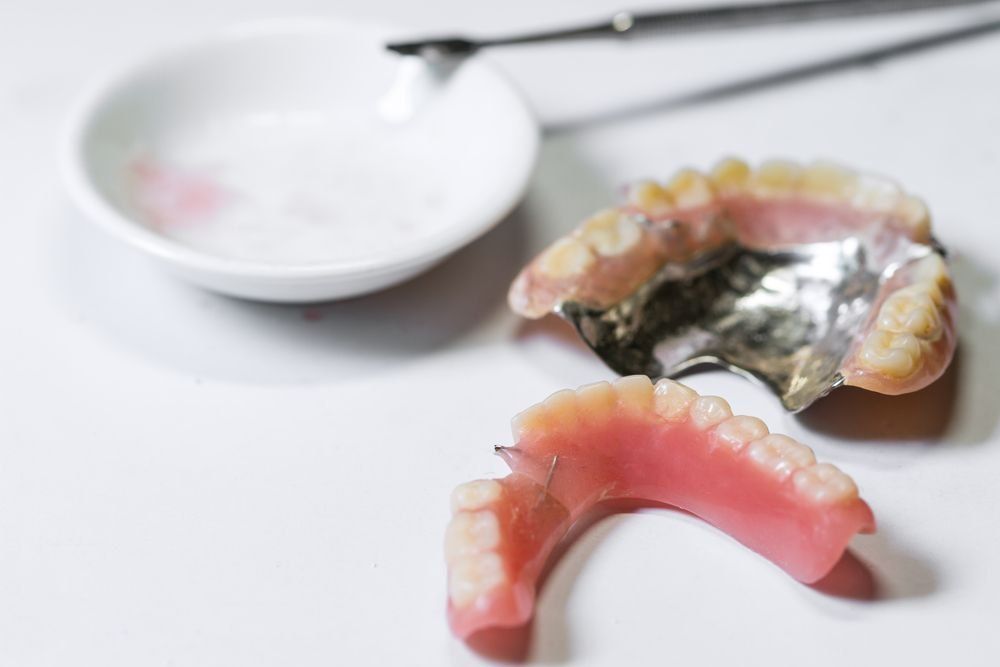 A Denture is Sitting on a Table Next to a Bowl of Toothpaste — Complete Denture Clinic in Kanwal, NSW