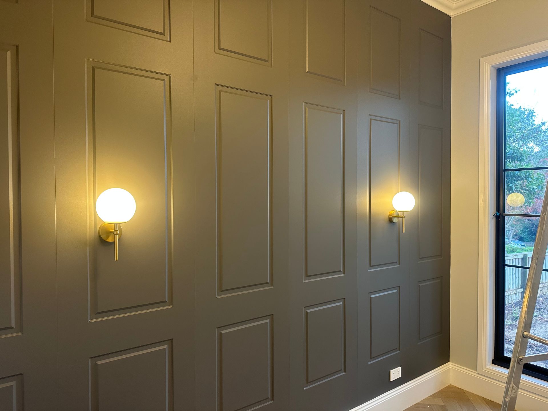 Grey panelled wall with two globe lights, a window, and a ladder — SparkSafe Electrical in Gerringong, NSW