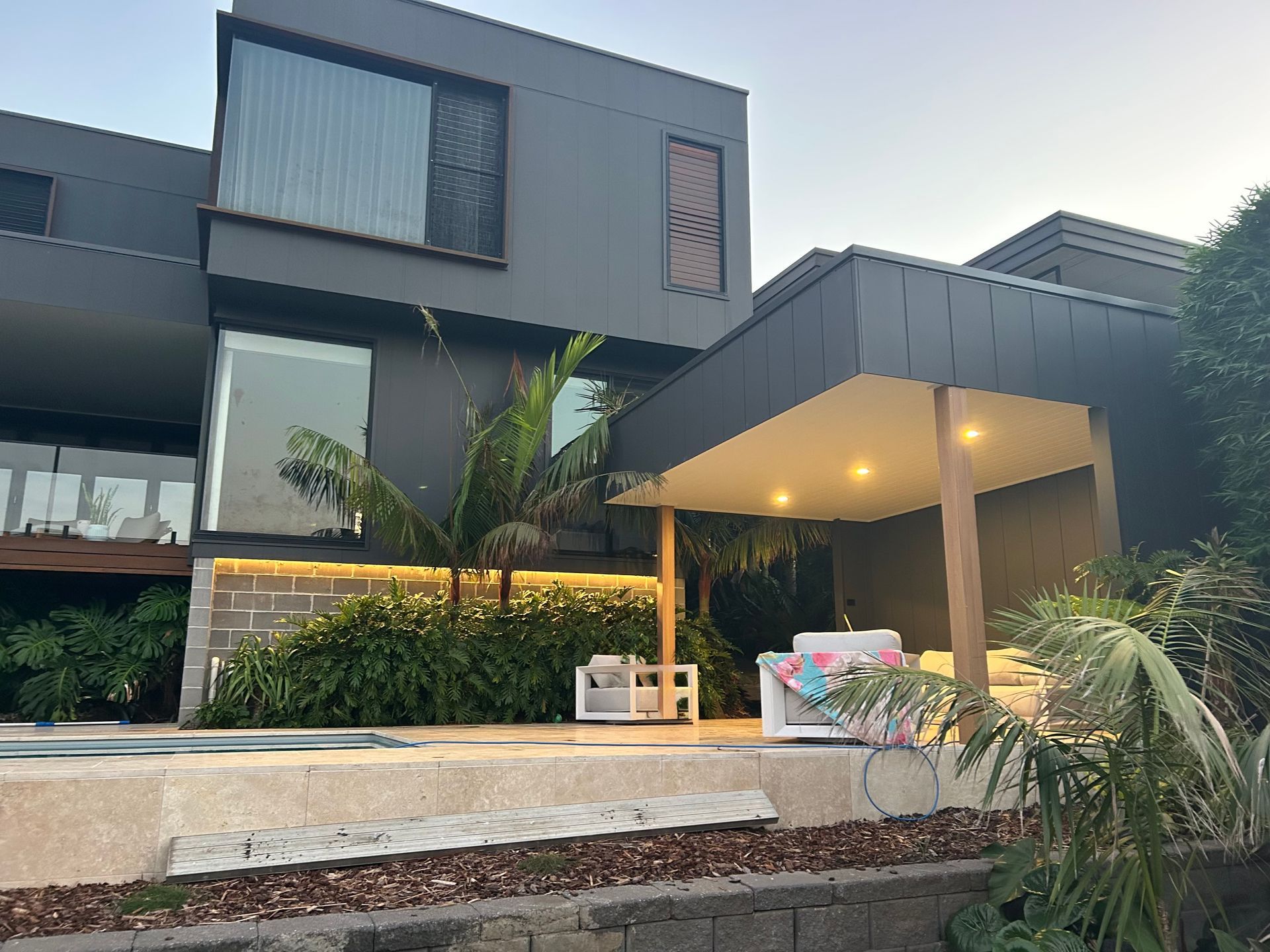 Modern Gray House With a Covered Entry, Warm Lights, and Lush Tropical Landscaping — SparkSafe Electrical in Bulli, NSW