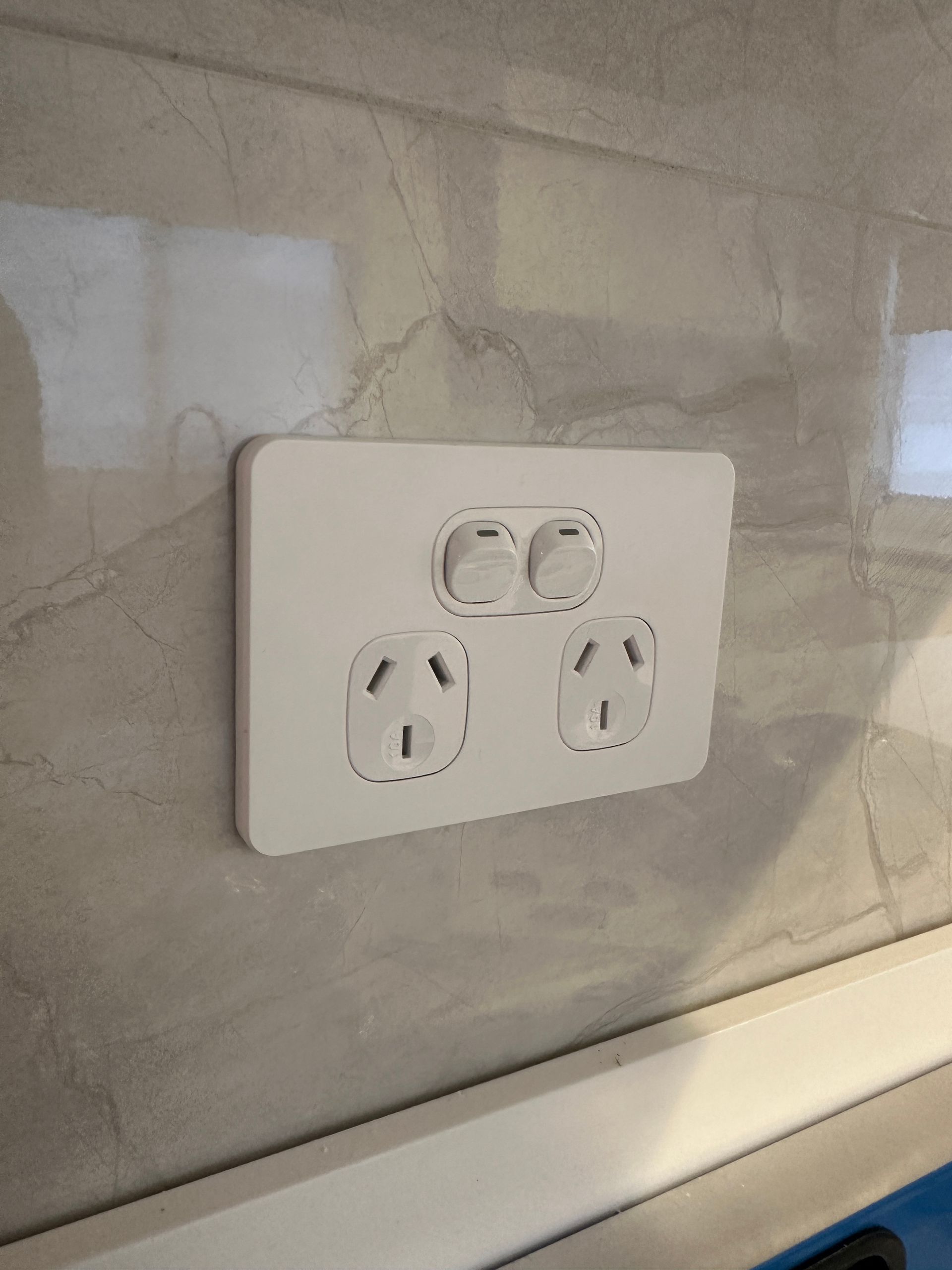 White electrical outlet with two switches on a marble-tiled wall — SparkSafe Electrical in Dapto, NSW