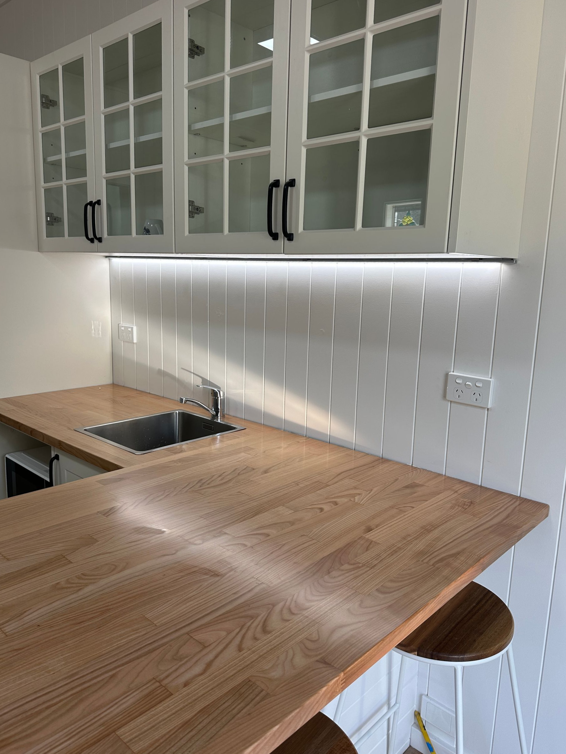 Kitchen with white cabinets, wooden countertops, sink, and bar stools  - SparkSafe Electrical in Dapto, NSW