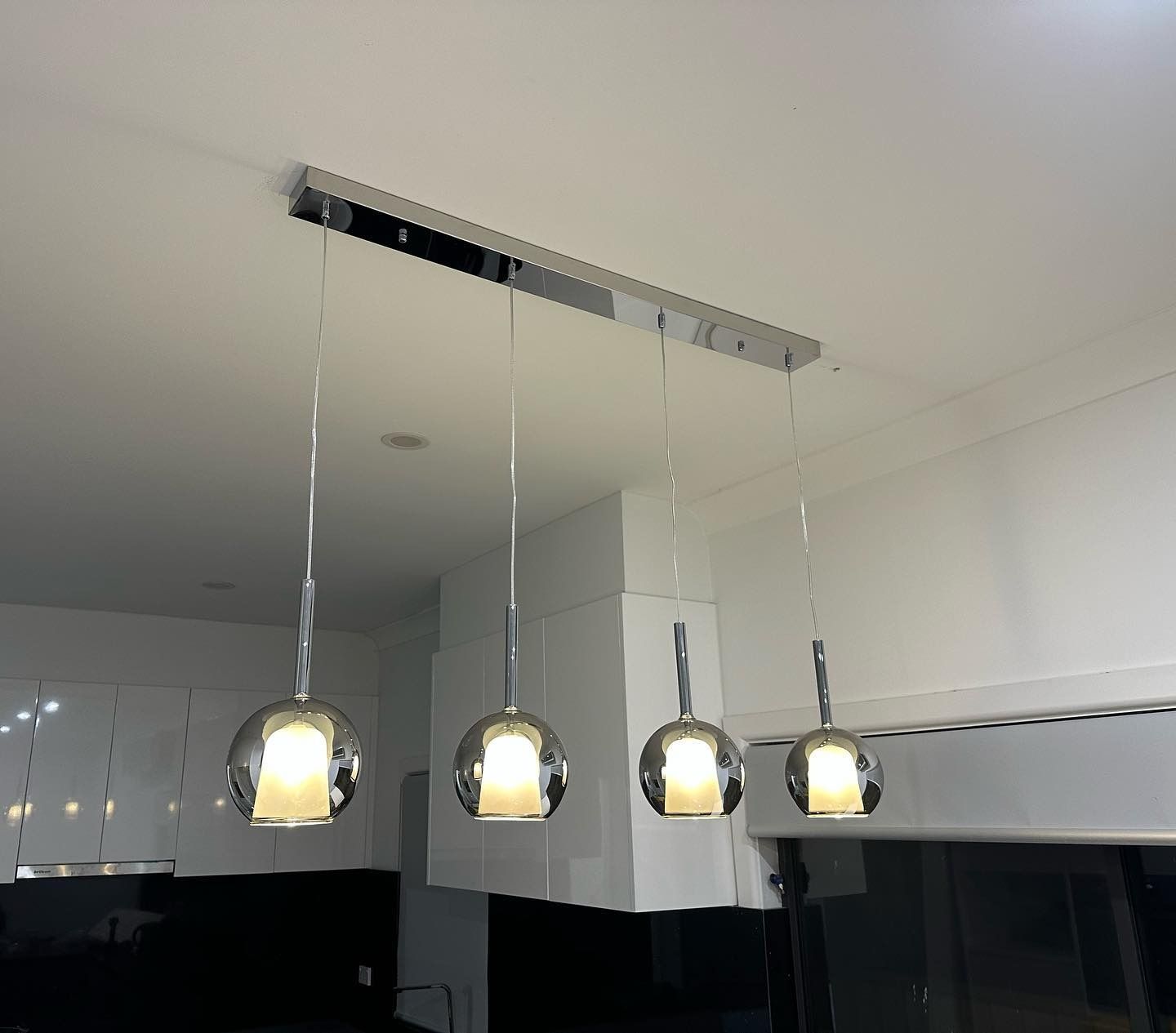 Four chrome globe pendant lights hanging from a ceiling, above a kitchen counter — SparkSafe Electrical in Dapto, NSW