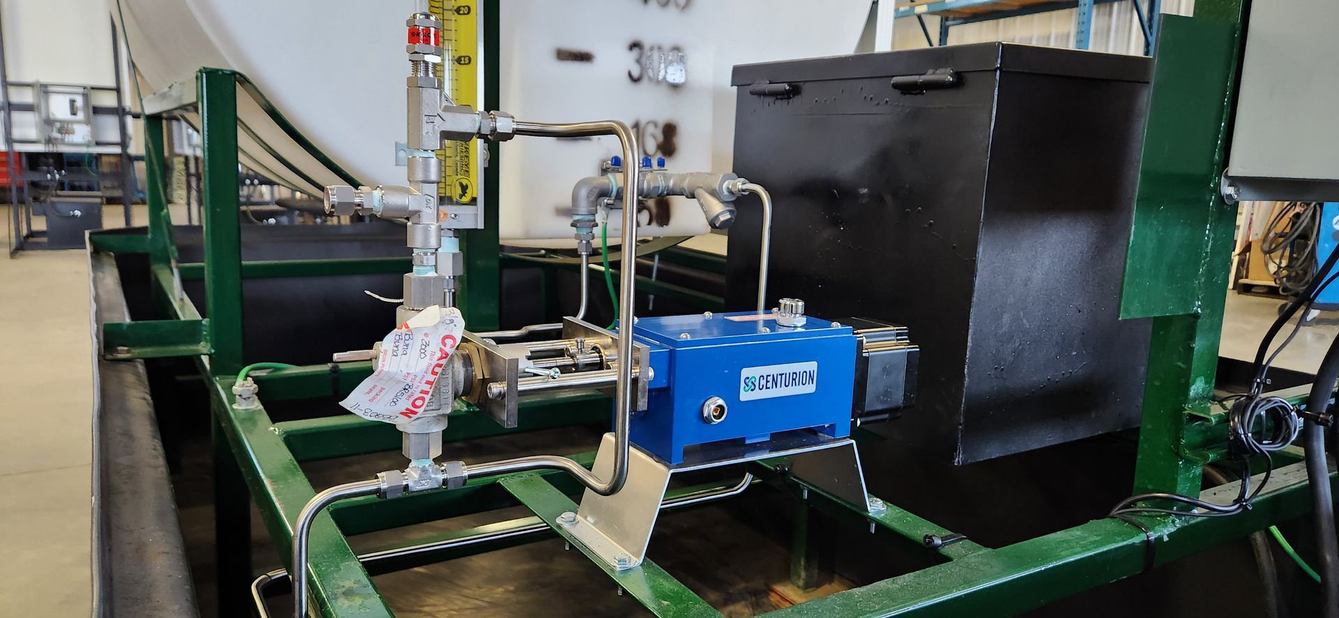 Industrial equipment setup with pipes, gauges, and a blue box. Green and black frame in a workshop.