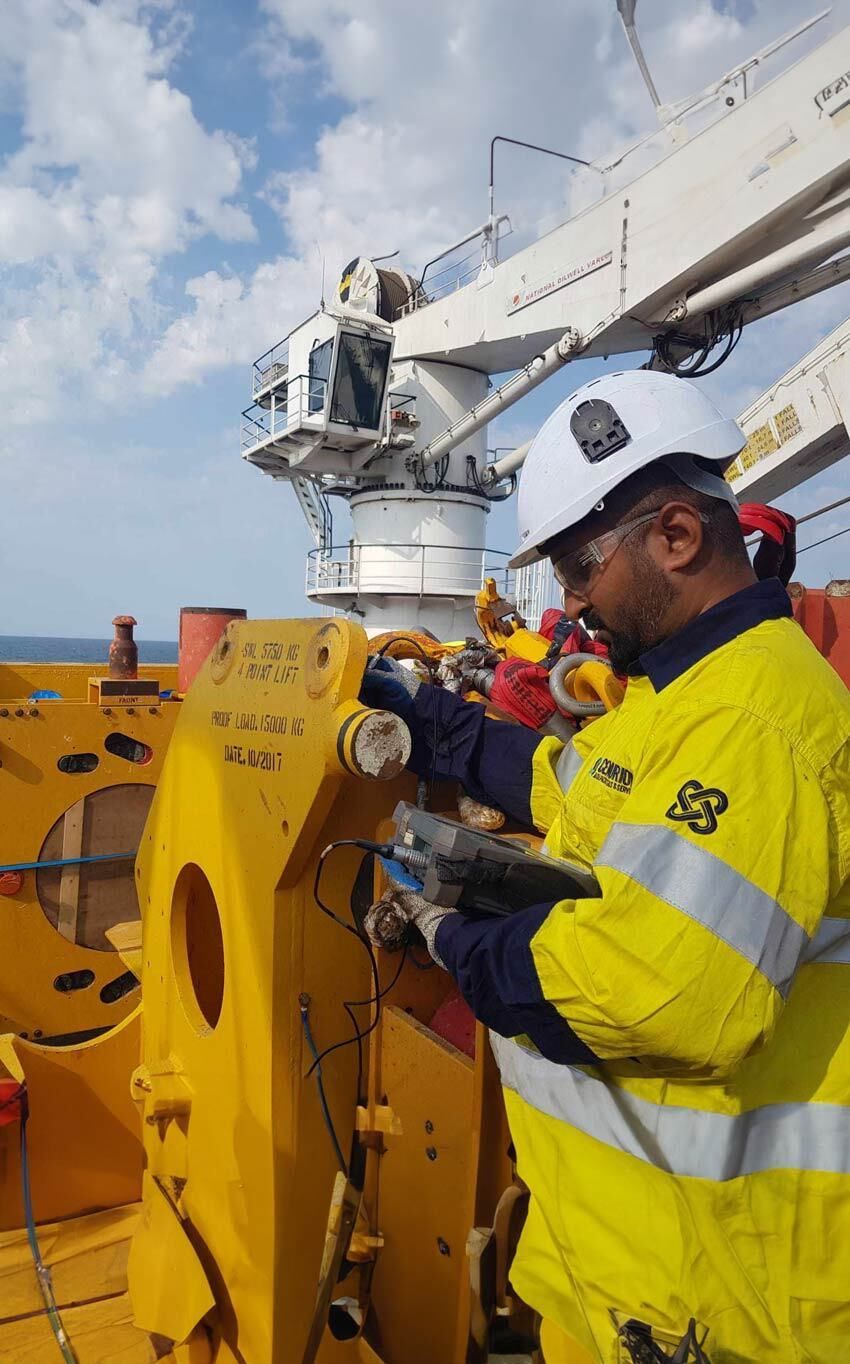 Workers in yellow safety gear inspect equipment on an offshore platform under a cloudy sky