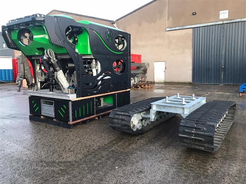 Black and green industrial robot on tracks outside a building.