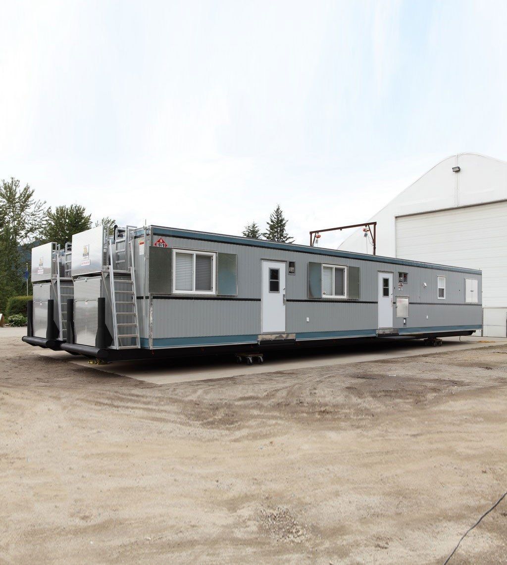 Gray modular building with white doors and windows, on gravel.